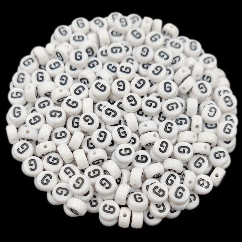 A close-up view of small white acrylic alphabet letter beads scattered on a dark background.