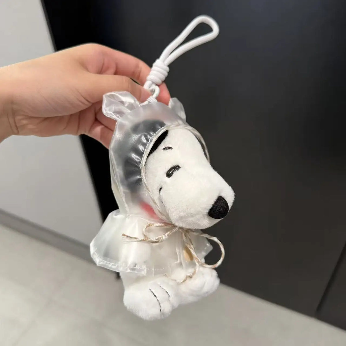 A white Snoopy plush keychain charm is being held by a hand against a dark background.