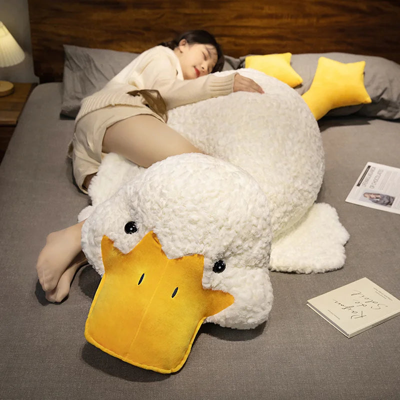 A woman is relaxing on a couch with a large yellow and white plush duck pillow.