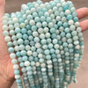 A hand holds a strand of light blue and white natural amazonite beads for jewelry making