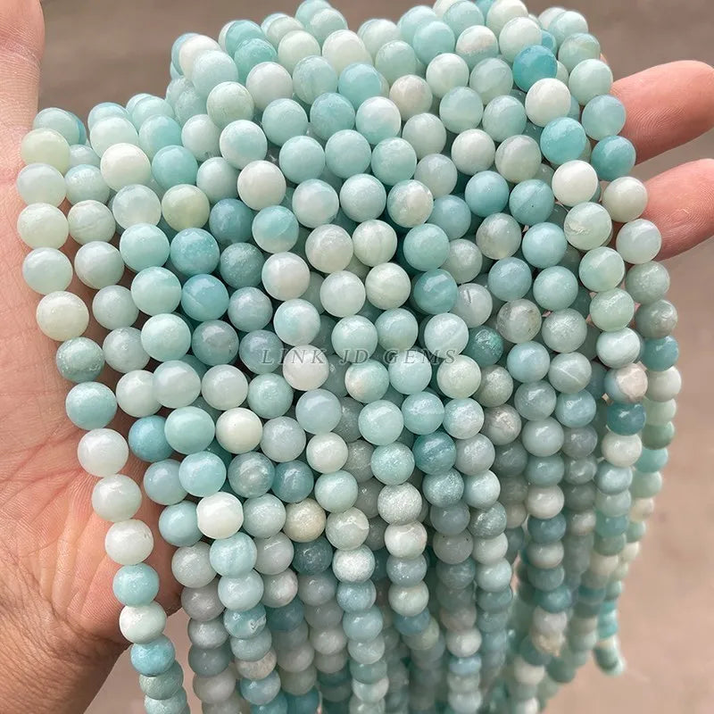 A hand holds a strand of light blue and white natural amazonite beads for jewelry making