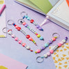 A collection of heart-shaped beaded keychains featuring various letters and words like Dad, Love, Mummy, Sweet, and Hugs.