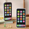 A white smartphone displaying an interactive baby learning app interface with colorful icons and music notes on a wooden tabl