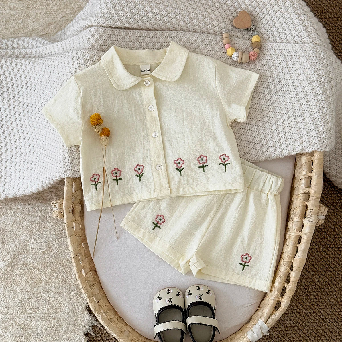 A cream baby cotton shirt and shorts set with a pink flower pattern displayed on a knitted surface.