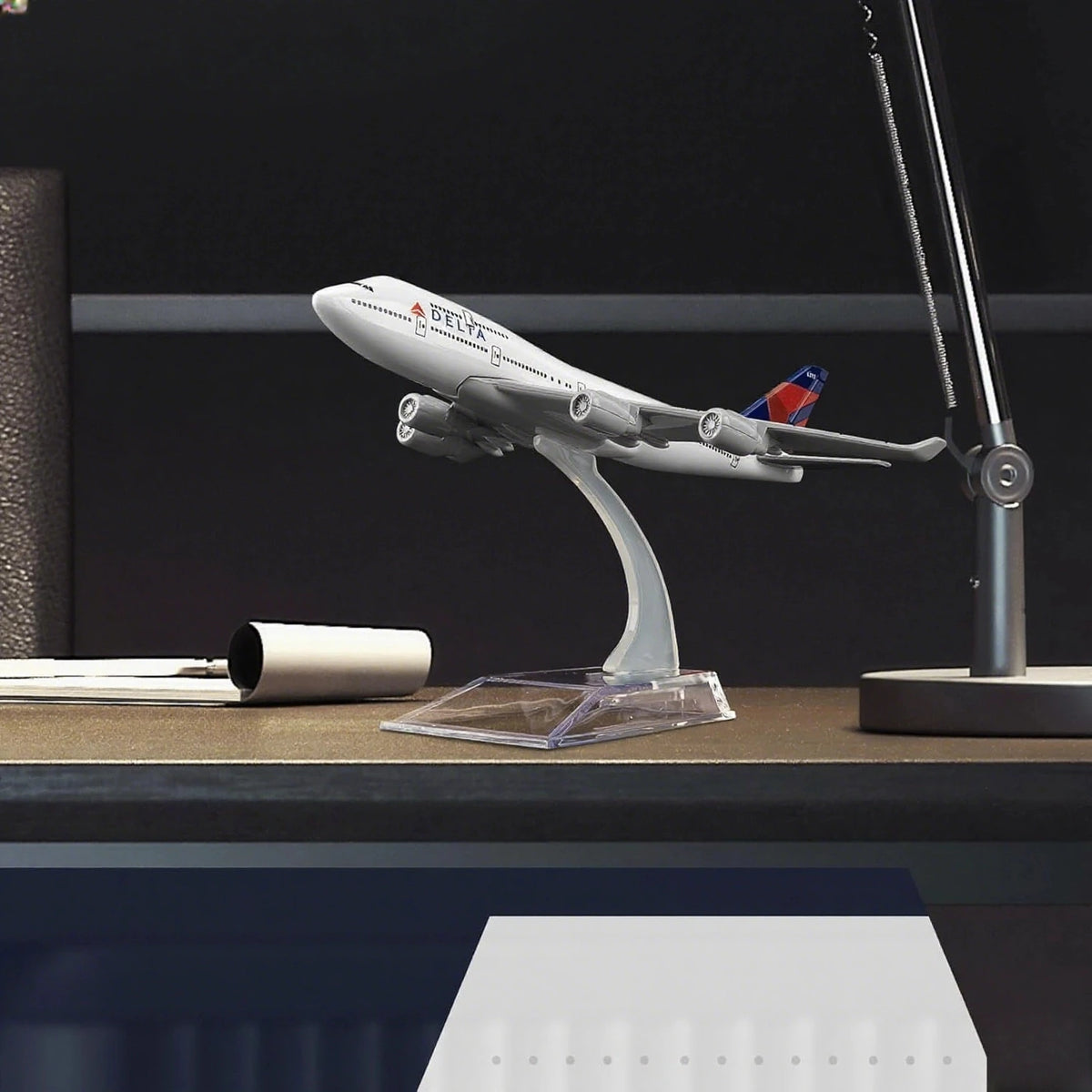 A silver and white Boeing 747 diecast model airplane is displayed on a desk next to a lamp.