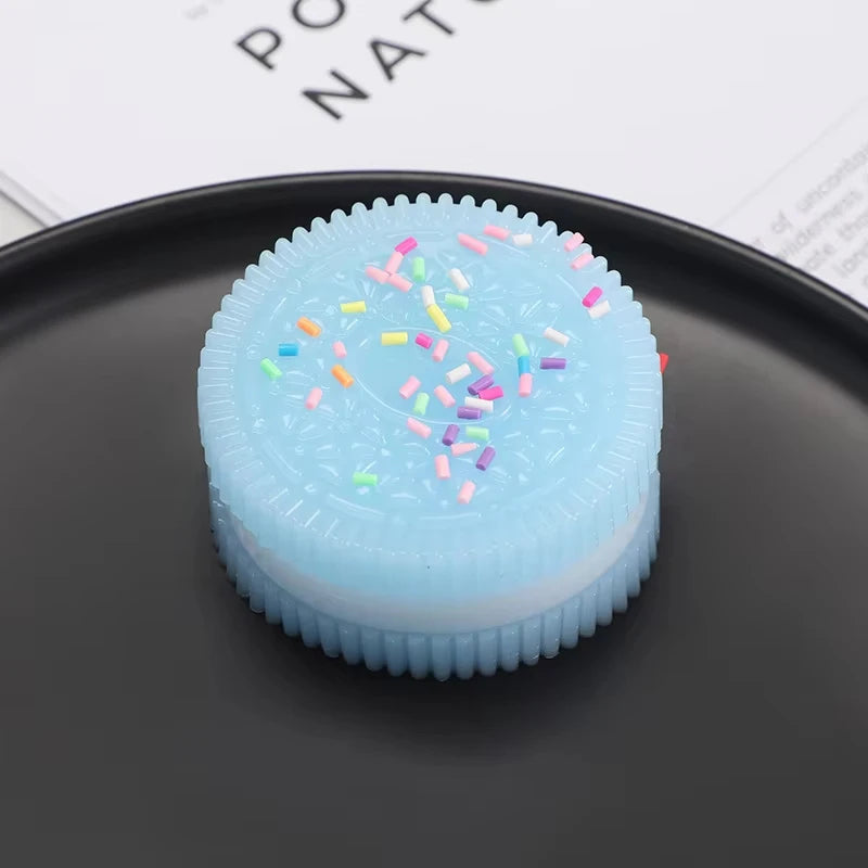A light blue biscuit squishy stress relief toy with colorful sprinkles resting on a dark gray plate.