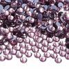 A close-up view of small, faceted purple and pink glass crystal rhinestones scattered on a white surface.