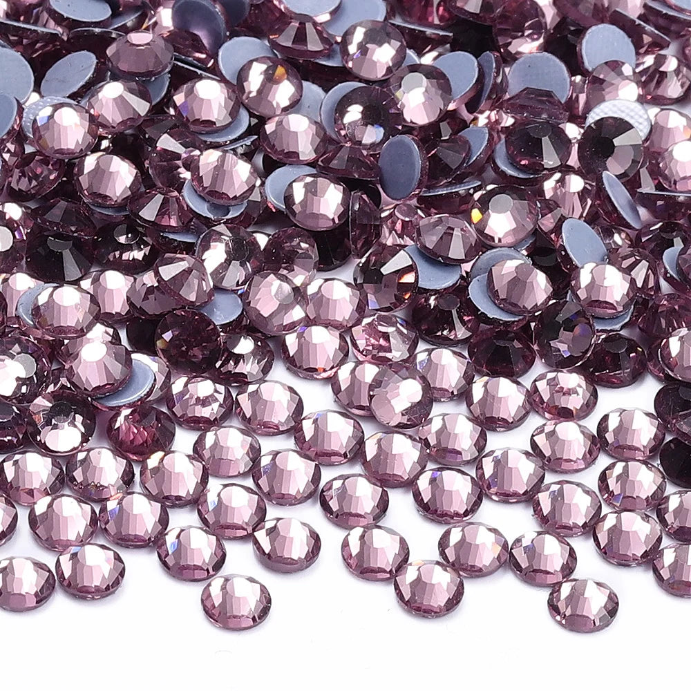 A close-up view of small, faceted purple and pink glass crystal rhinestones scattered on a white surface.
