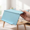 A hand holds a light blue foldable Mahjong card holder with a non-slip stand.