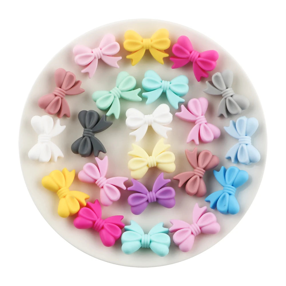 A collection of colorful silicone bow tie beads in various shades including pink, yellow, purple, and blue arranged on a whit