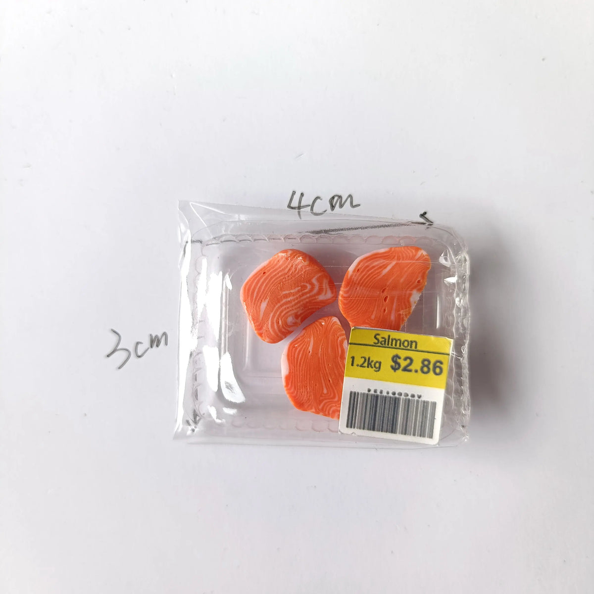 A clear plastic package containing three pieces of salmon meat labeled as 1.2kg for $2.86