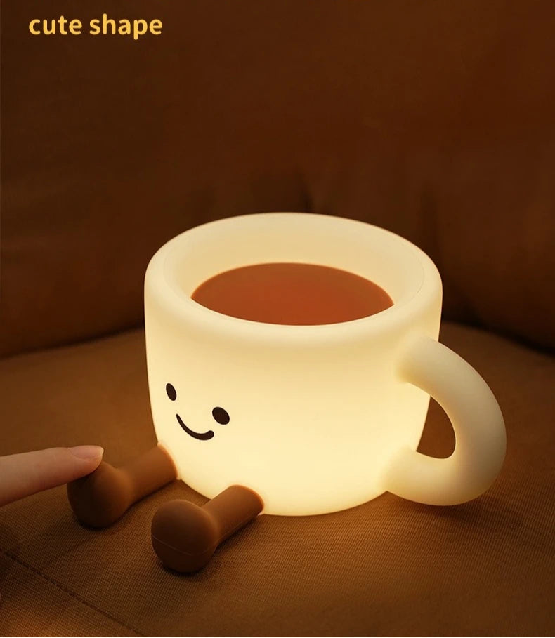 A cute, glowing coffee cup shaped night light with a smiling face rests on a brown surface.