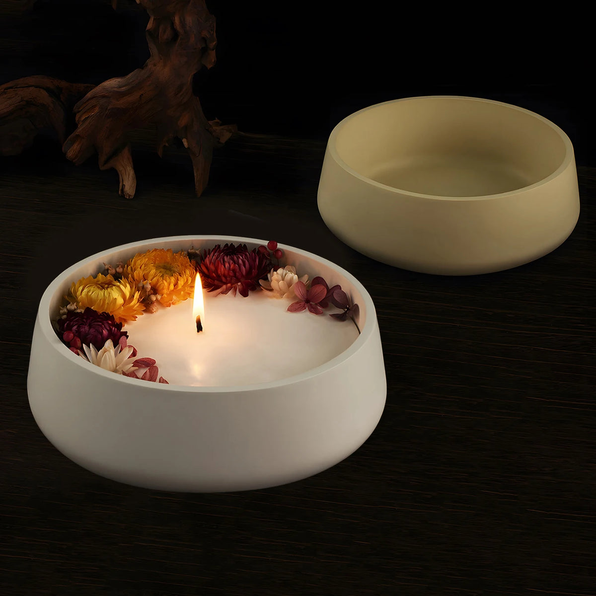 A white silicone mold candle in a round dish surrounded by dried flowers on a dark wooden surface.