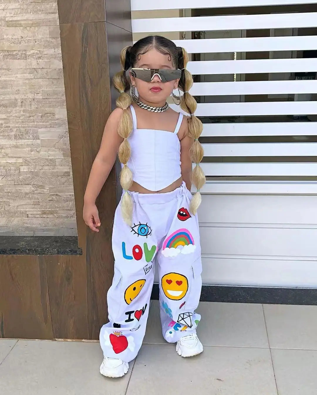A girl wearing a white two-piece outfit with a suspender top and long pants, accessorized with sunglasses and jewelry.