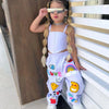 A young girl wearing a white two-piece outfit with suspender top and long pants, accessorized with sunglasses and jewelry.