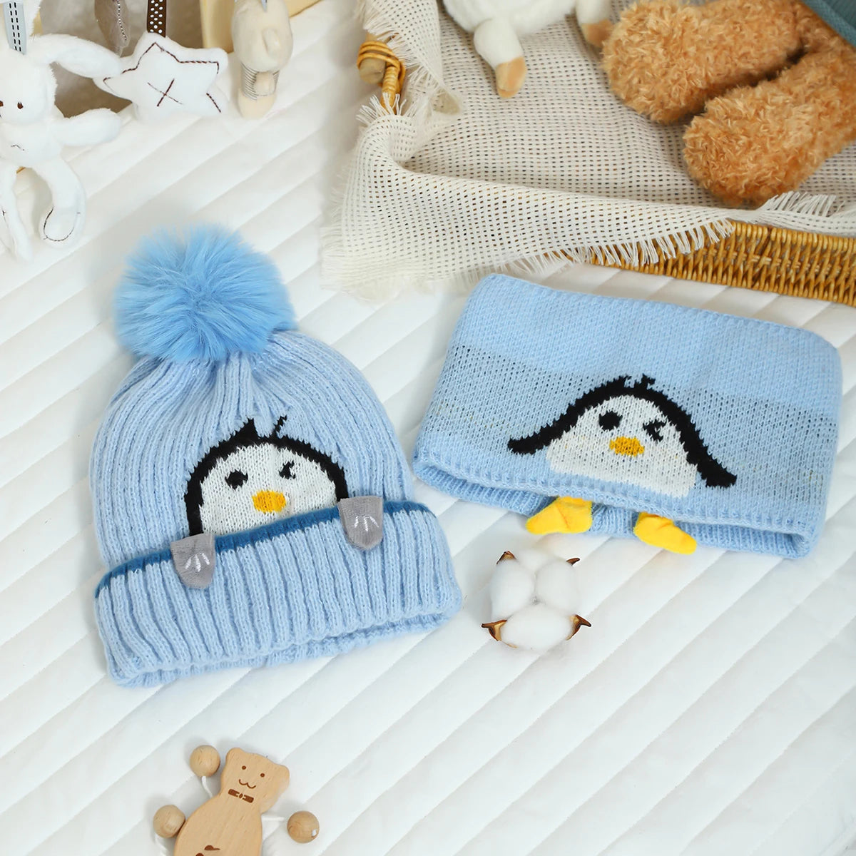 A knitted blue penguin hat and scarf set with white accents resting on a white surface.