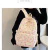 Un sac à dos blanc avec un motif de nœud rose porté par une personne devant un mur clair.