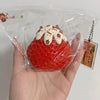 A hand holds a red strawberry squeeze fidget toy with white icing details inside clear plastic packaging.