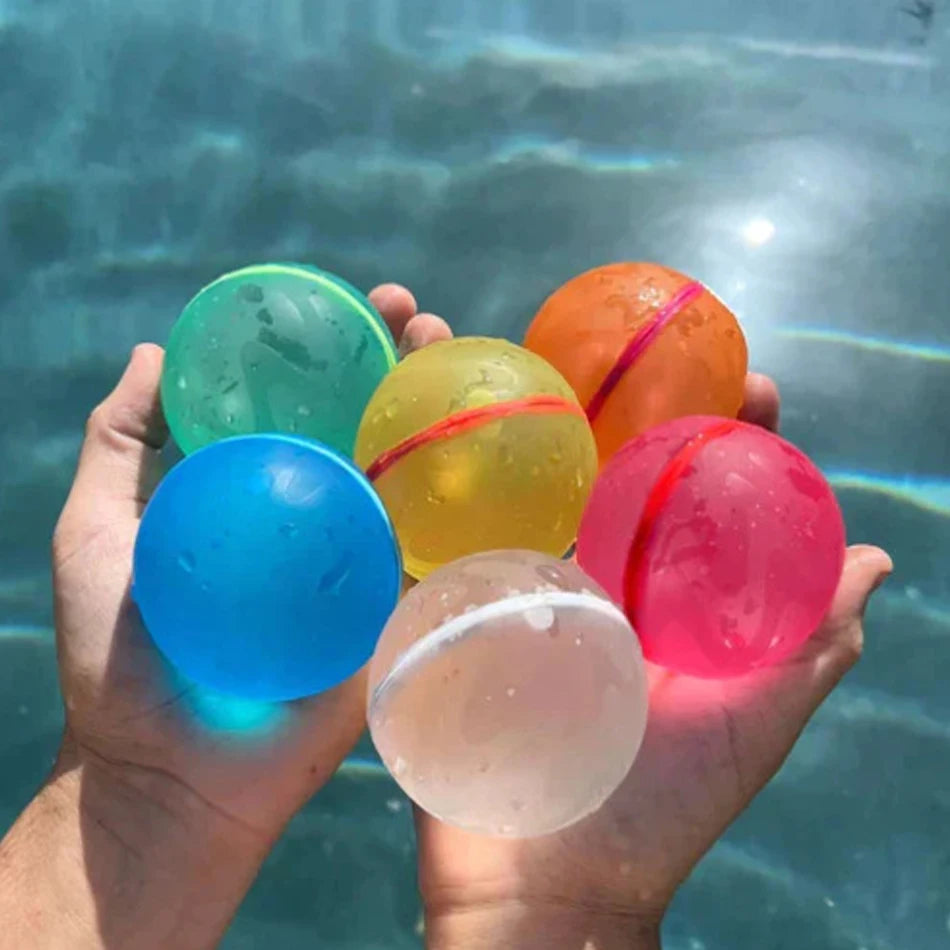 A hand holds several colorful reusable water balloons including green, yellow, orange, blue, and pink spheres in clear water.