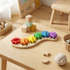 A wooden Montessori busy board for toddlers featuring colorful gears, switches, and sensory elements on a light wood table.