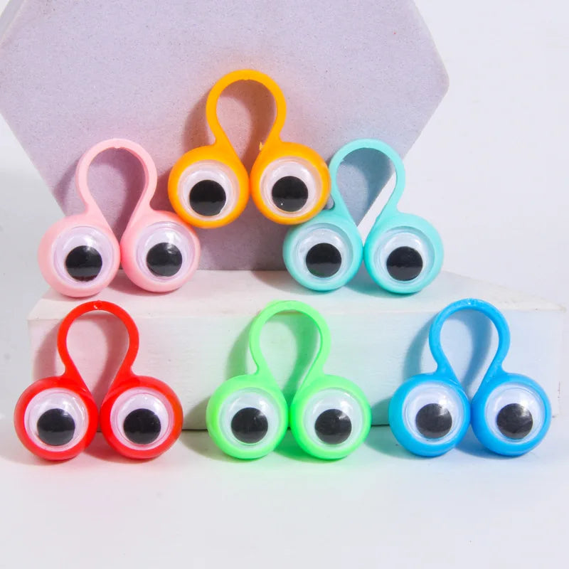 A collection of colorful wiggle eye finger rings in pink, orange, teal, and green, displayed on a white surface.