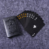 A black playing card deck with a gold-colored sequence of cards and an Ace of clubs is displayed on a gray fabric background.