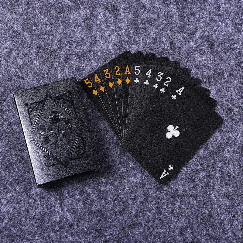 A black playing card deck with a gold-colored sequence of cards and an Ace of clubs is displayed on a gray fabric background.