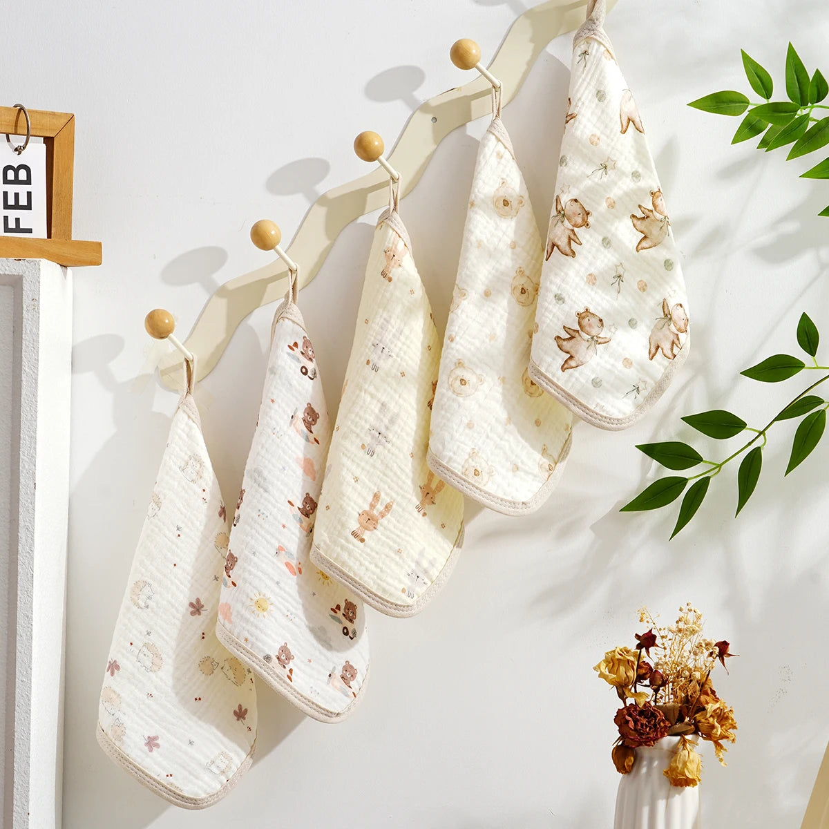 A set of five white and beige soft cotton muslin baby washcloths hanging on a wooden rack.