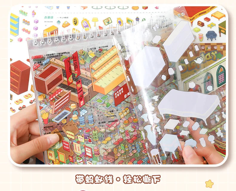 A hand holds an open sticker book featuring a detailed, colorful scene of a tiny DIY pocket cabin or village.