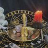 A brass pentagram altar plate holds a lit candle, crystals, and ritual parchments on a dark surface.