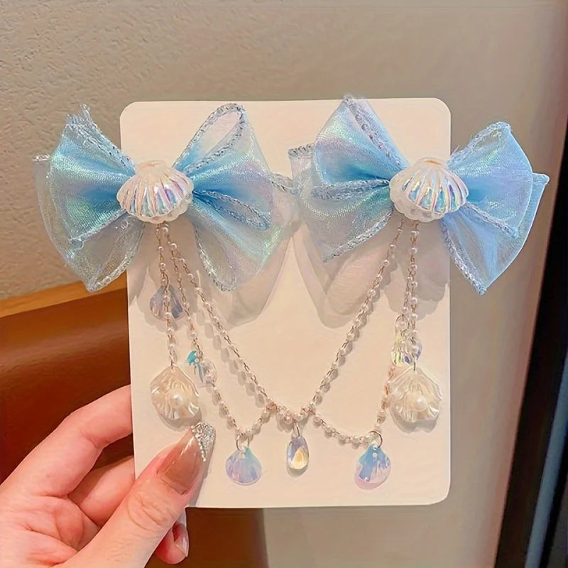 A pair of light blue mermaid princess hair clips featuring iridescent fabric bows and dangling pearl-like beads.