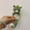 A handmade green crocheted otter rattle and teether ring attached to a wooden loop.