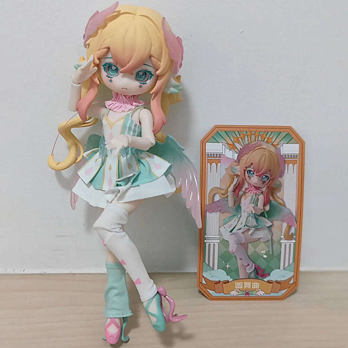 A light pink and white articulated ball-jointed doll with long blonde hair and pink accents standing next to its packaging bo