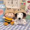 A plush toy of Snoopy with a dog-like face wearing a brown helmet sitting next to a white dog plush.