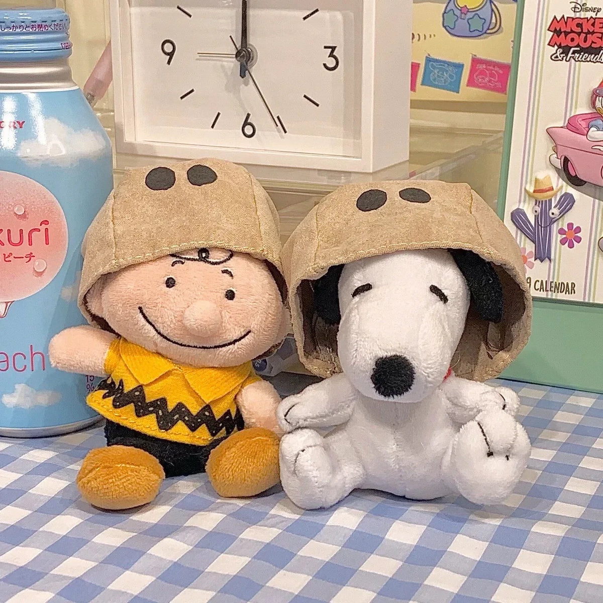 A plush toy of Snoopy with a dog-like face wearing a brown helmet sitting next to a white dog plush.