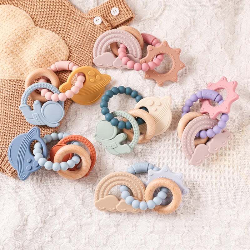 Assortment of food-grade silicone planet teethers in various pastel colors and shapes on a textured fabric.