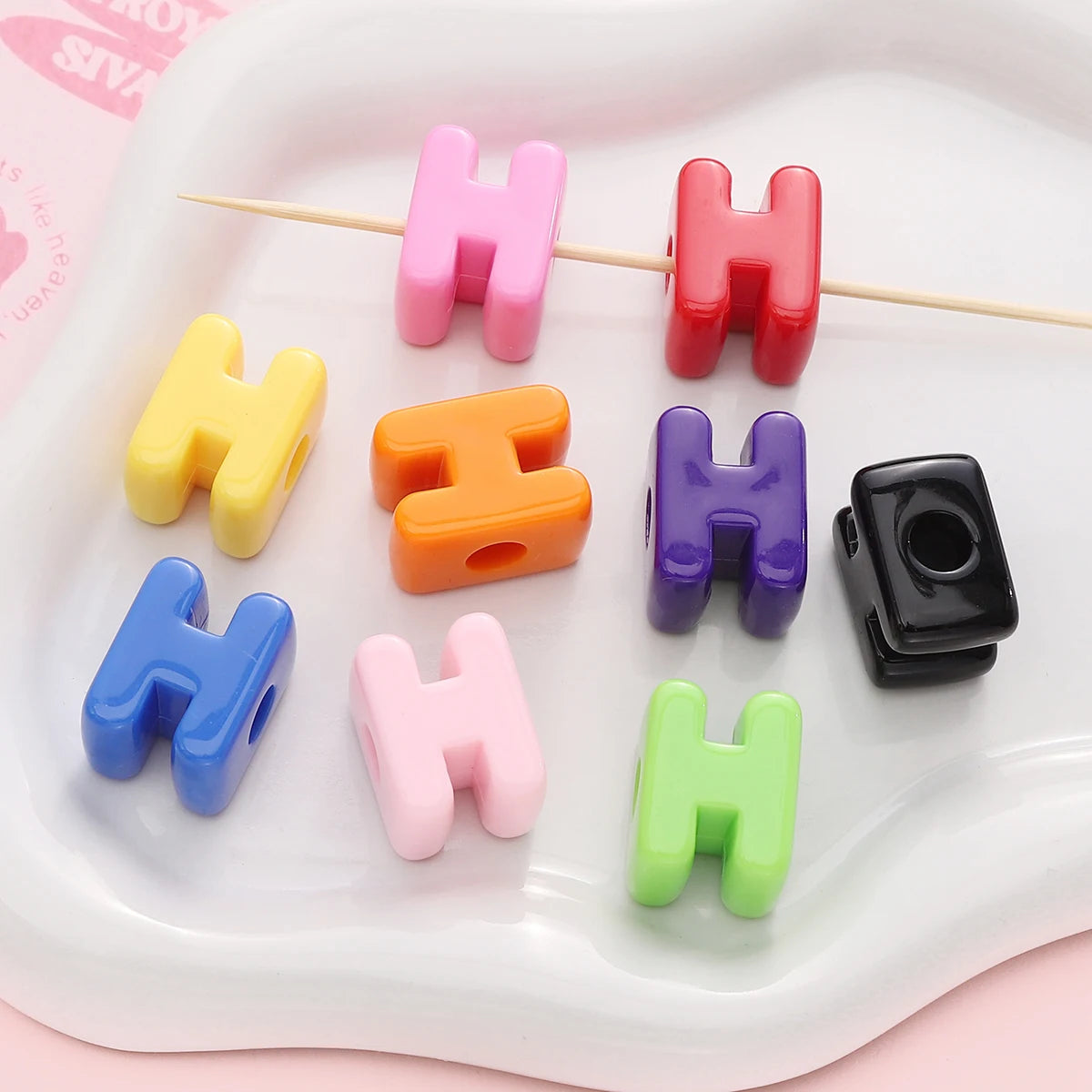 A collection of colorful acrylic letter beads shaped like the letter H arranged on a white tray.