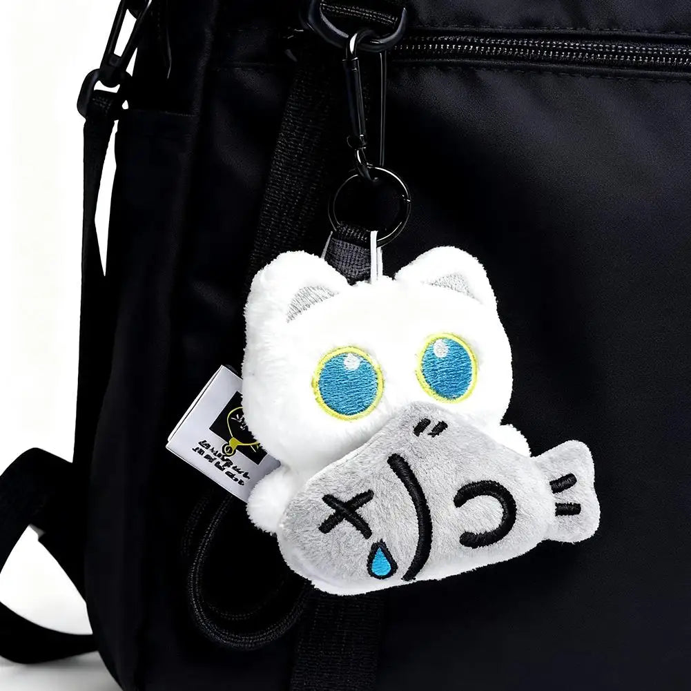 A white cat plush toy with blue eyes and a gray face is attached to a black backpack strap.