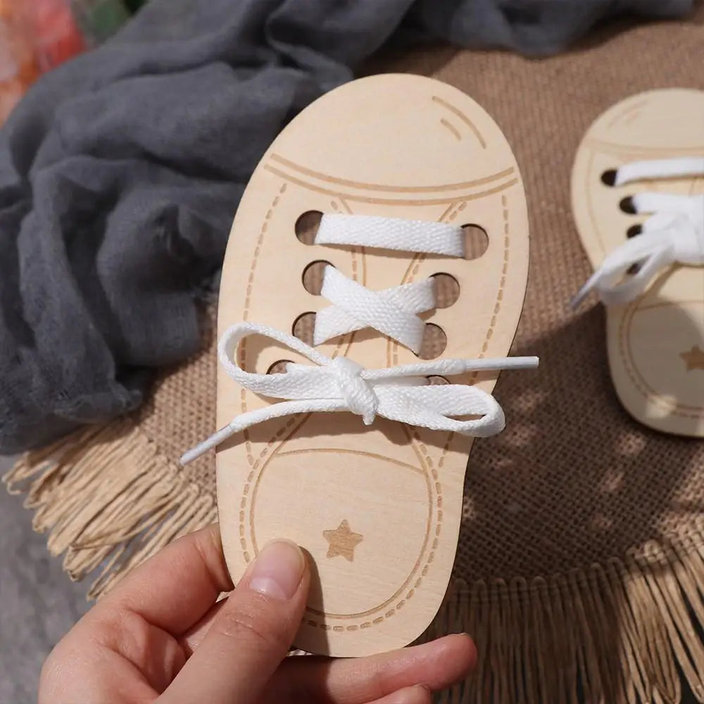 A hand holds a wooden lacing shoe toy for fine motor skills with white laces.