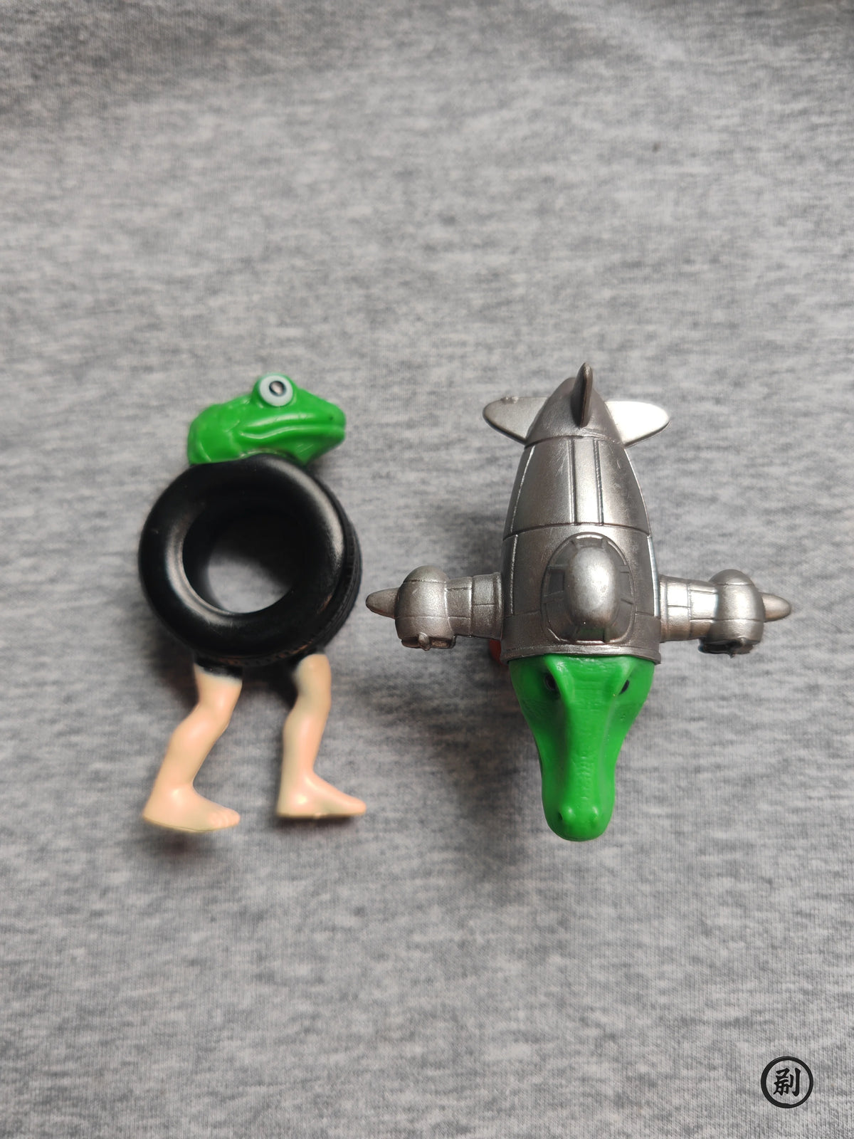 A set of two Italian Brainrot wooden stick doll figures, one green and one silver, against a gray background.