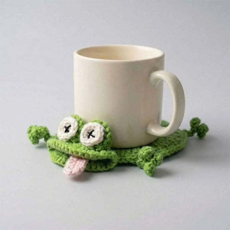 A handmade crochet lizard coaster sits next to a cream-colored mug on a light gray surface.