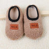 Pair of beige plush baby slippers with black trim and WLS brand tags