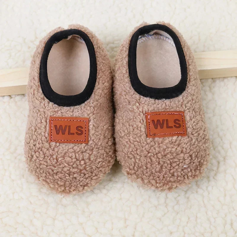 Pair of beige plush baby slippers with black trim and WLS brand tags