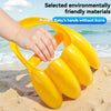 A hand is holding a yellow dinosaur claw sand digging toy on a sandy beach near the ocean.