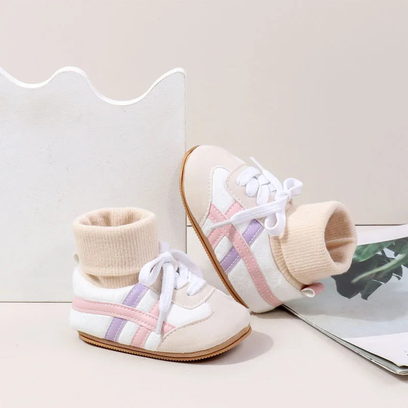 A pair of light beige and pink ankle-hugging baby booties with white laces and anti-slip soles.