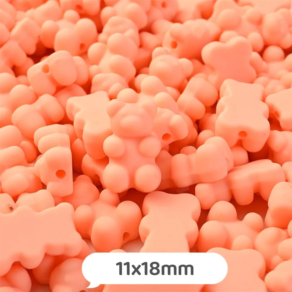 A close-up of small, pink bear-shaped acrylic craft beads with a shimmer finish scattered on a surface.