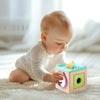 A baby is interacting with a wooden tissue box toy designed for fine motor skills.