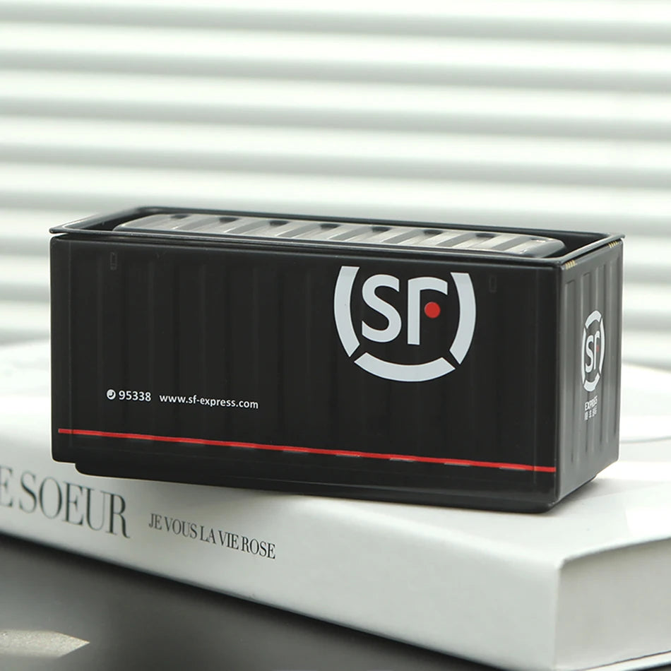 Black miniature industrial iron storage box with a white logo and lid resting on a white book.