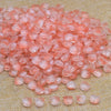 A pile of translucent pink tulip flower glass beads scattered on a beige fabric surface.