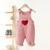 Pink corduroy toddler overalls with a red heart embroidery hanging on a wooden rack